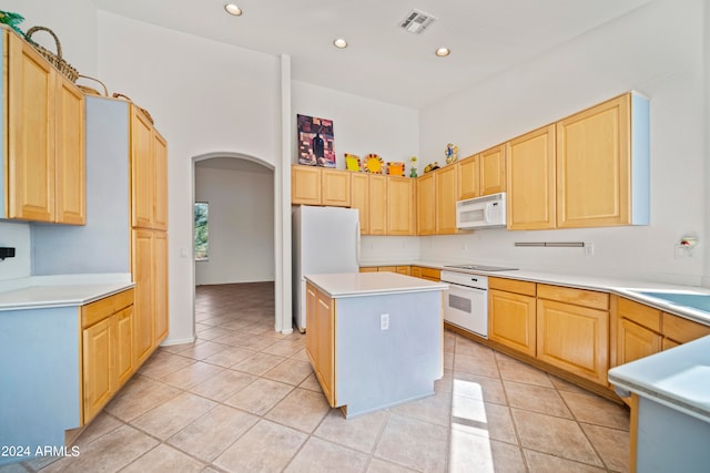 kitchen featuring light brown cabinetry, white appliances, a center island, and light tile patterned floors