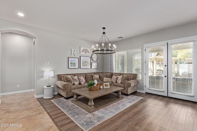 living room featuring light wood-style flooring, french doors, arched walkways, baseboards, and a chandelier