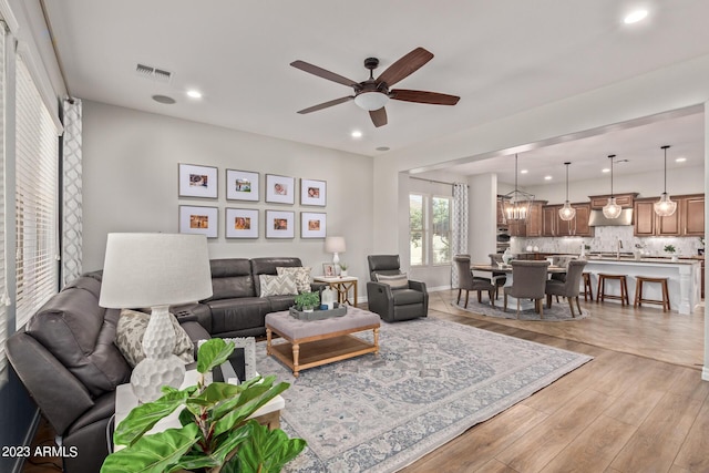 living area with light wood-type flooring, visible vents, ceiling fan with notable chandelier, recessed lighting, and baseboards