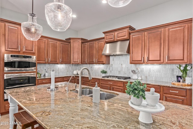 kitchen with under cabinet range hood, light stone counters, a sink, appliances with stainless steel finishes, and decorative backsplash
