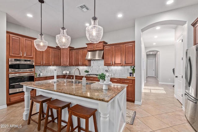 kitchen with visible vents, under cabinet range hood, a sink, arched walkways, and appliances with stainless steel finishes