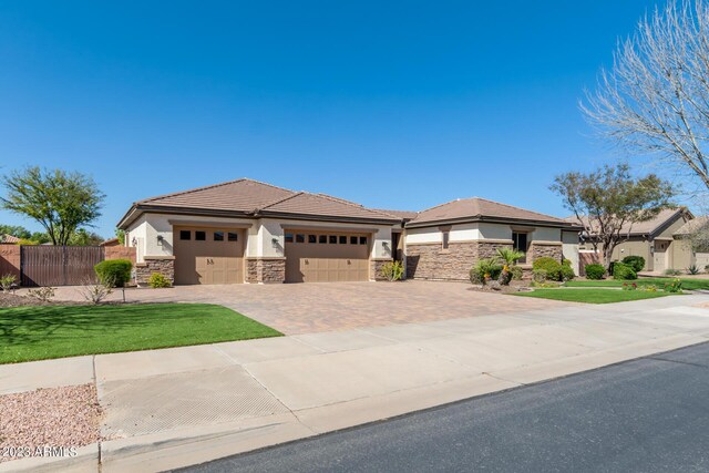 prairie-style home with fence, an attached garage, stucco siding, stone siding, and decorative driveway