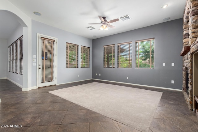 unfurnished living room with ceiling fan, a stone fireplace, and dark tile patterned floors