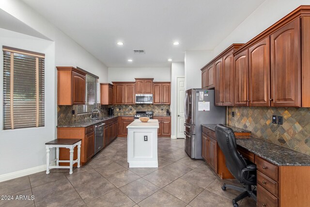 kitchen featuring decorative backsplash, tile patterned floors, stainless steel appliances, sink, and built in desk