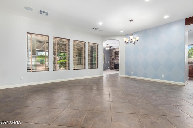 empty room with a fireplace and ceiling fan with notable chandelier