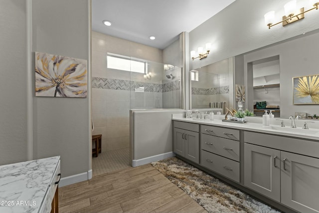 bathroom with double vanity, walk in shower, a sink, and wood finished floors