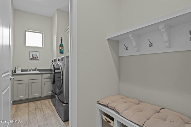 washroom with a sink, cabinet space, washing machine and dryer, and light wood-style flooring