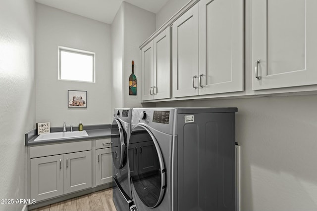 laundry room featuring cabinet space, washer and dryer, light wood-style floors, and a sink