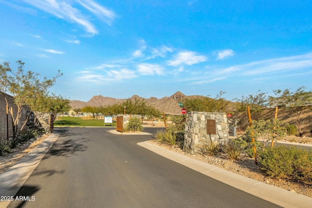 view of road featuring a gated entry, traffic signs, a mountain view, and curbs