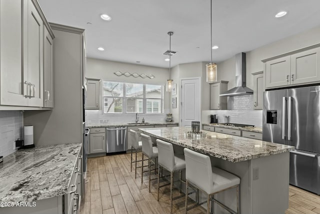 kitchen with wall chimney exhaust hood, a kitchen island, appliances with stainless steel finishes, light wood-style flooring, and gray cabinetry