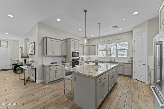 kitchen with gray cabinetry, a sink, visible vents, appliances with stainless steel finishes, and light wood-type flooring