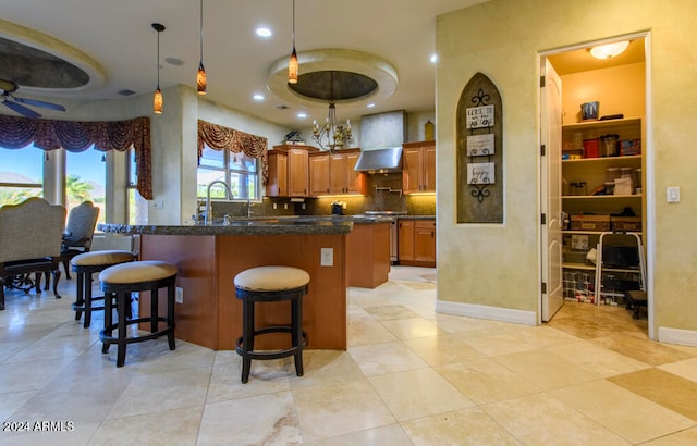 kitchen featuring ceiling fan, wall chimney range hood, a kitchen breakfast bar, pendant lighting, and a kitchen island