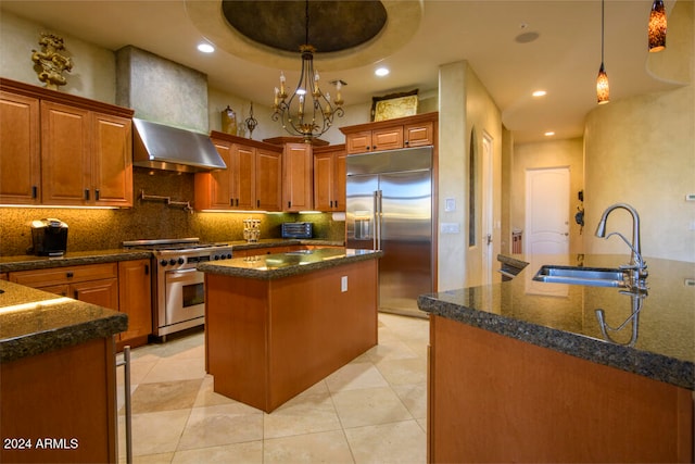 kitchen featuring premium appliances, a tray ceiling, a kitchen island with sink, wall chimney range hood, and pendant lighting