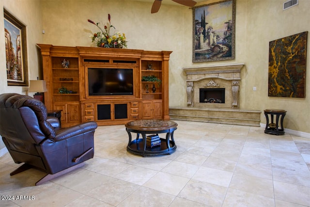 living room featuring ceiling fan, a towering ceiling, a high end fireplace, and light tile patterned flooring