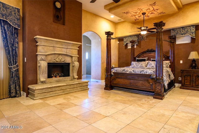 tiled bedroom with ceiling fan, a towering ceiling, and a premium fireplace