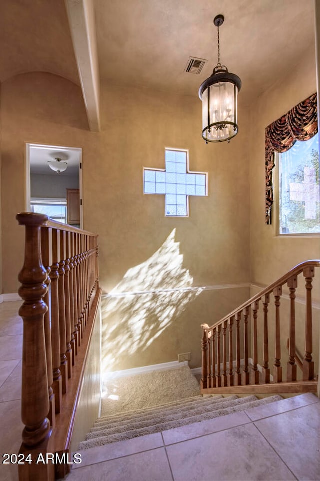 stairway featuring a chandelier, beam ceiling, tile patterned floors, and a healthy amount of sunlight