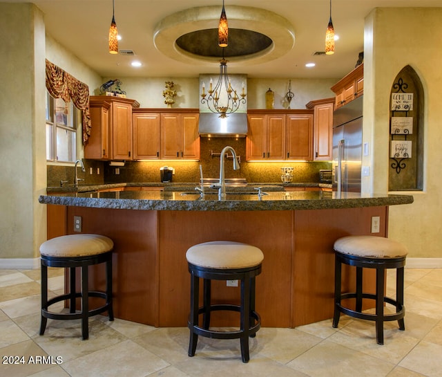 kitchen with a breakfast bar area, decorative backsplash, decorative light fixtures, and stainless steel built in refrigerator