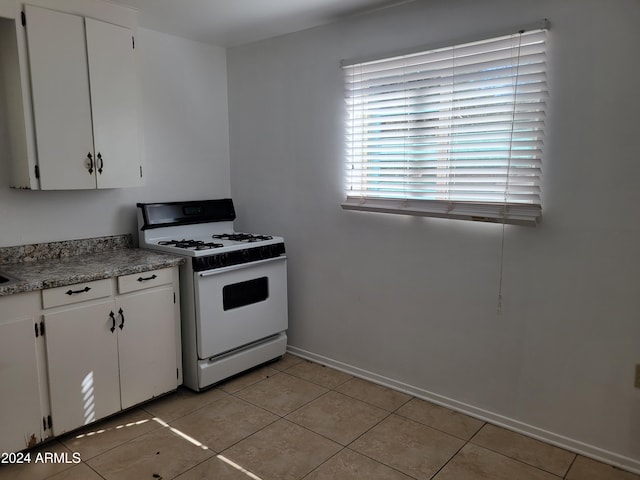 kitchen with white gas stove, white cabinetry, and light tile patterned floors