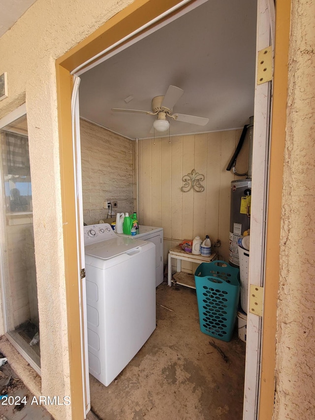 clothes washing area with wooden walls, washing machine and dryer, water heater, and ceiling fan