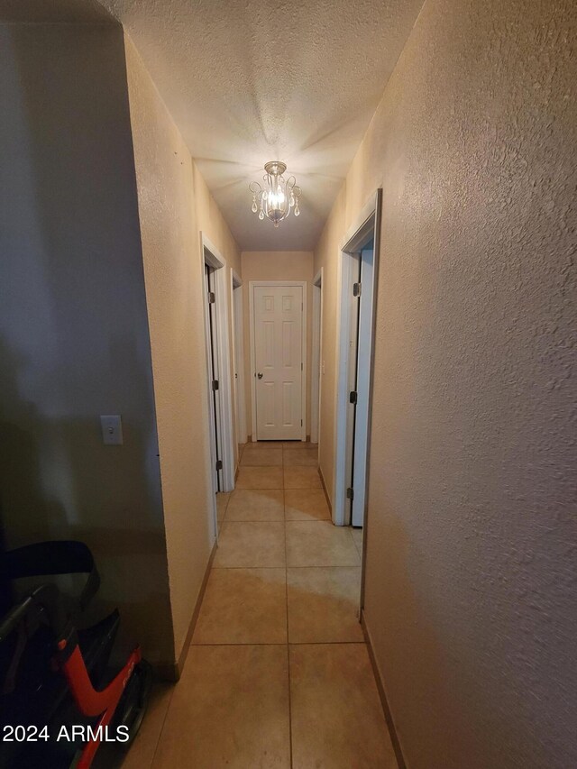 corridor featuring a textured ceiling, a notable chandelier, and light tile patterned floors