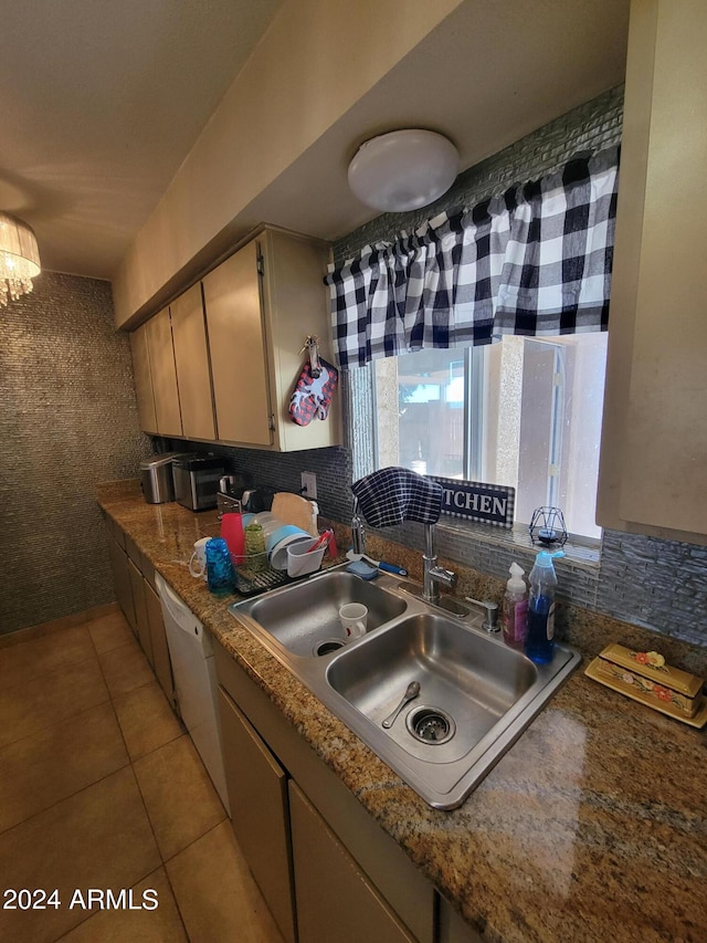 kitchen featuring dark stone countertops, tasteful backsplash, light tile patterned floors, white dishwasher, and sink