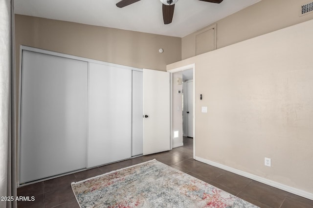 unfurnished bedroom featuring dark tile patterned flooring, a closet, and ceiling fan