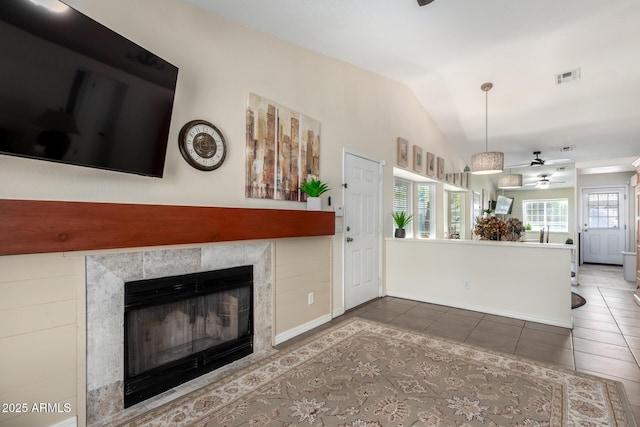 unfurnished living room with dark tile patterned floors, a tile fireplace, lofted ceiling, and a wealth of natural light