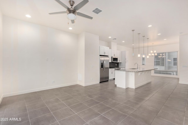 kitchen with white cabinets, hanging light fixtures, light stone countertops, an island with sink, and stainless steel appliances