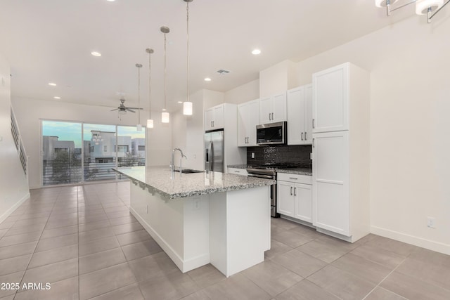 kitchen with appliances with stainless steel finishes, sink, pendant lighting, white cabinets, and an island with sink