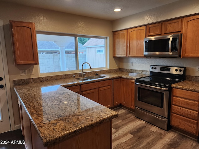 kitchen featuring dark stone counters, stainless steel appliances, wood-type flooring, and sink