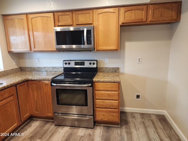 kitchen with appliances with stainless steel finishes, light wood-type flooring, and light stone counters