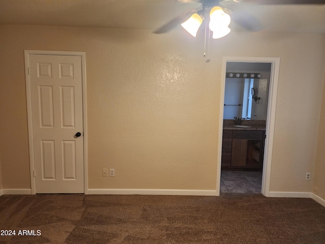 empty room with dark colored carpet, ceiling fan, and sink