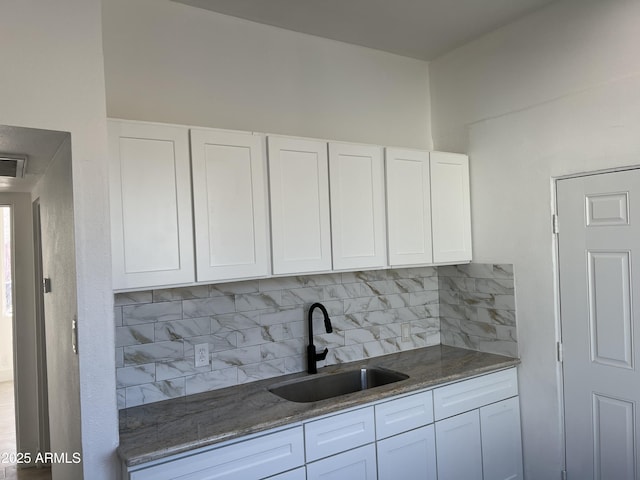 kitchen featuring tasteful backsplash, stone counters, a sink, and white cabinets