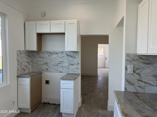 kitchen with wood finished floors, white cabinets, a wealth of natural light, light stone countertops, and tasteful backsplash