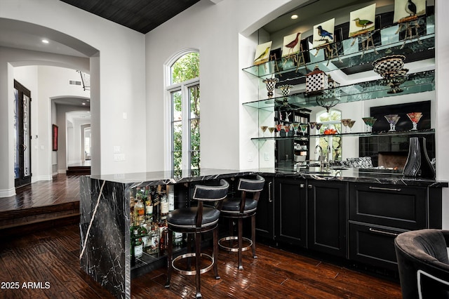 bar with dark stone countertops, sink, and dark wood-type flooring