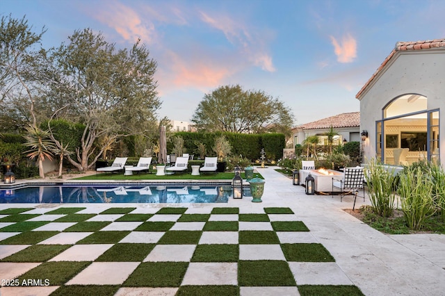 pool at dusk with a patio and a fire pit