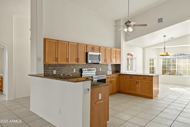 kitchen featuring light tile patterned floors, stainless steel appliances, tasteful backsplash, dark stone counters, and a peninsula