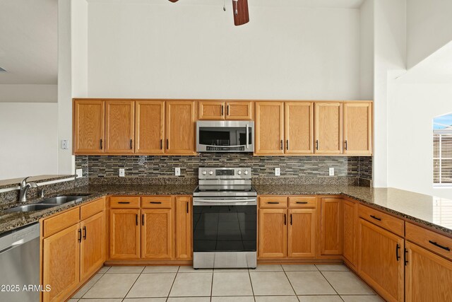 kitchen with stainless steel appliances, a high ceiling, a sink, dark stone counters, and a peninsula