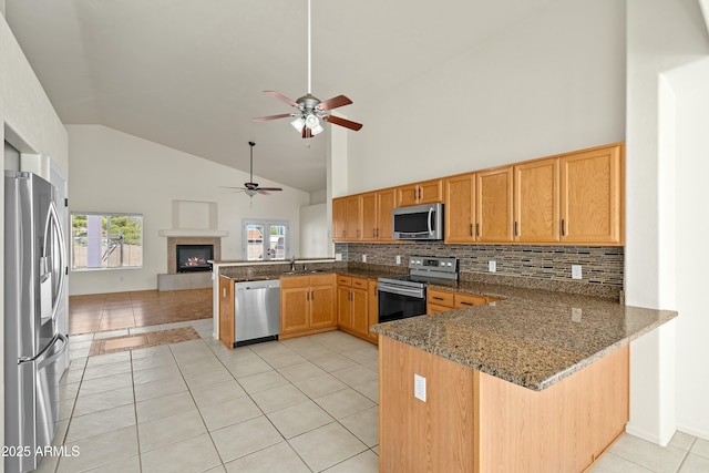 kitchen with light tile patterned floors, a peninsula, a fireplace, appliances with stainless steel finishes, and dark stone counters