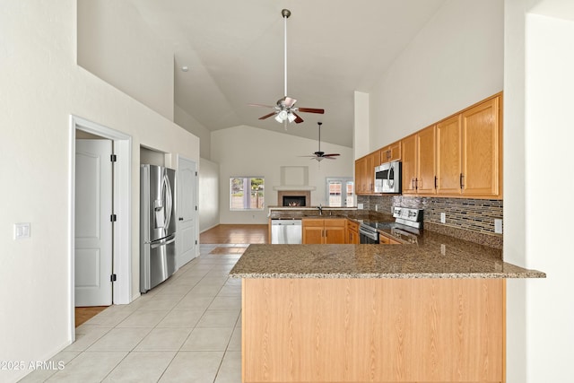 kitchen featuring light tile patterned floors, tasteful backsplash, appliances with stainless steel finishes, dark stone countertops, and a peninsula