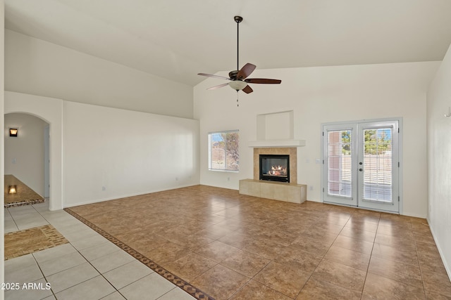 unfurnished living room featuring light tile patterned floors, ceiling fan, arched walkways, high vaulted ceiling, and a fireplace