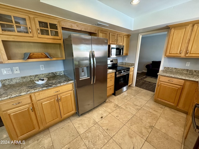 kitchen with visible vents, brown cabinetry, glass insert cabinets, appliances with stainless steel finishes, and dark stone countertops