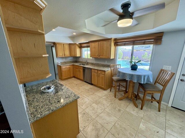 kitchen featuring a raised ceiling, light stone countertops, stainless steel appliances, and ceiling fan