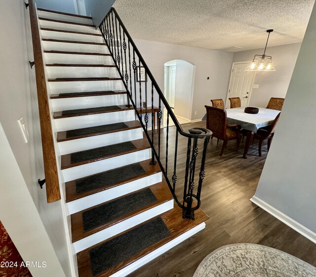 staircase with a textured ceiling, an inviting chandelier, and hardwood / wood-style floors