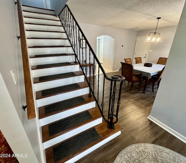 stairs featuring arched walkways, a textured ceiling, wood finished floors, and baseboards