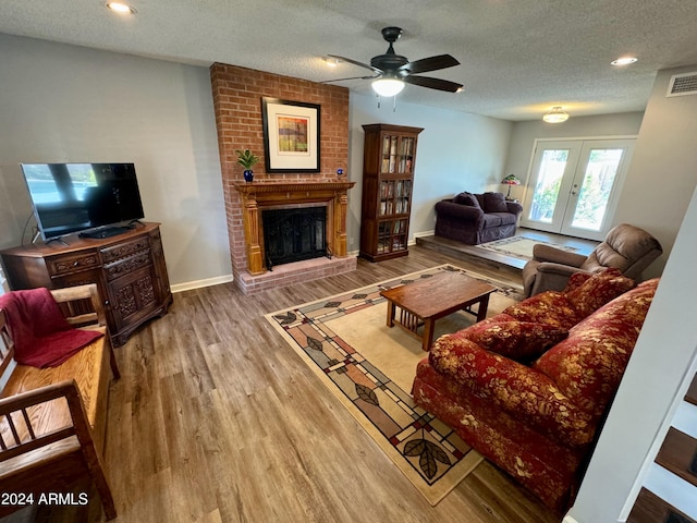 living room featuring baseboards, wood finished floors, a textured ceiling, french doors, and a fireplace