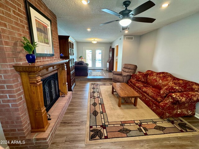 living room featuring a fireplace, french doors, wood-type flooring, ceiling fan, and a textured ceiling