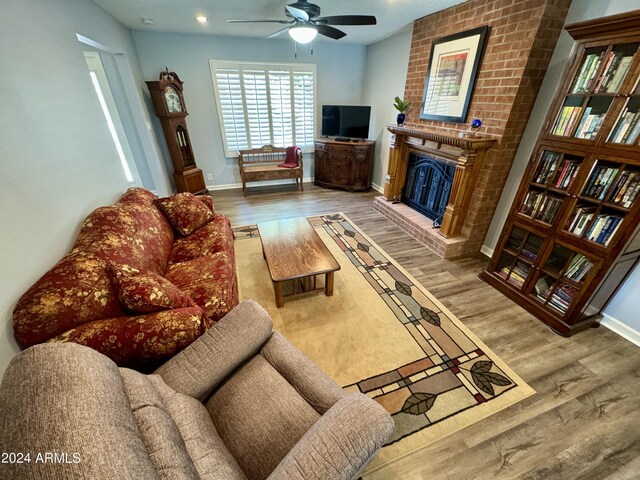 living room featuring hardwood / wood-style floors, ceiling fan, a fireplace, and brick wall