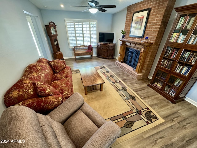 living room with a ceiling fan, a brick fireplace, baseboards, and wood finished floors