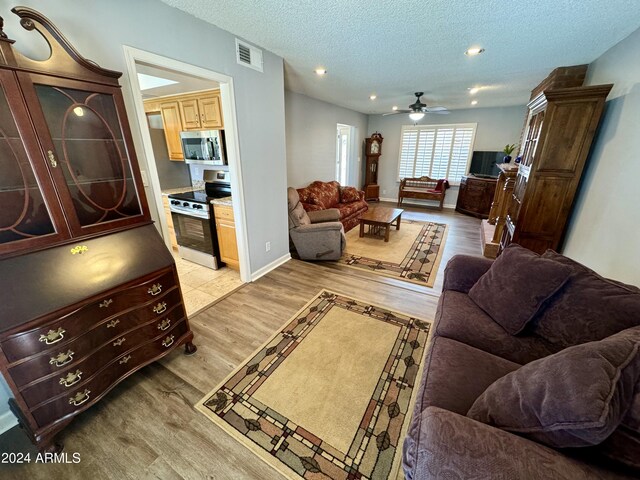 living room featuring light wood-type flooring, a textured ceiling, and ceiling fan